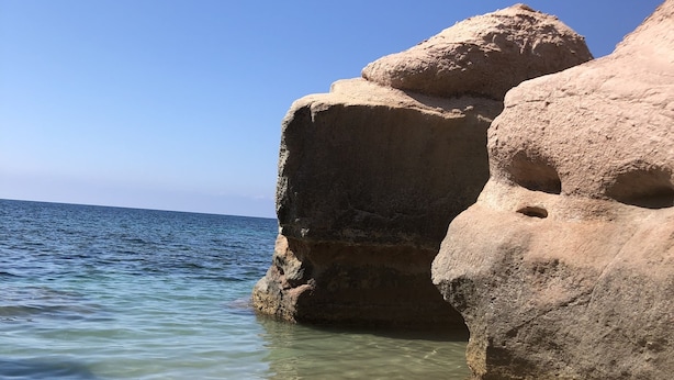 Une plage à l’eau claire, bordée de grandes formations rocheuses.
