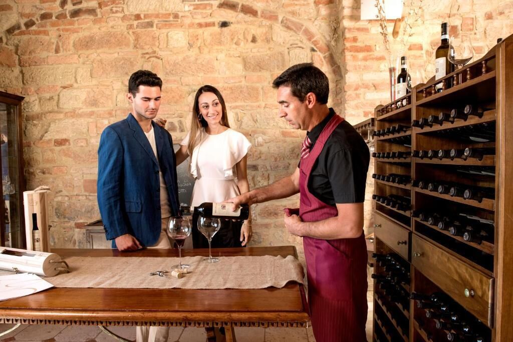 Ein Weinkostraum mit Backsteinwand, Weinkisten aus Holz und einem Tisch mit Weingläsern und einer Flasche.
