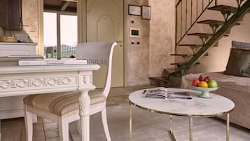 Una habitación con una silla blanca, una mesa redonda con tapa de mármol, una escalera y un frutero en el sofá.