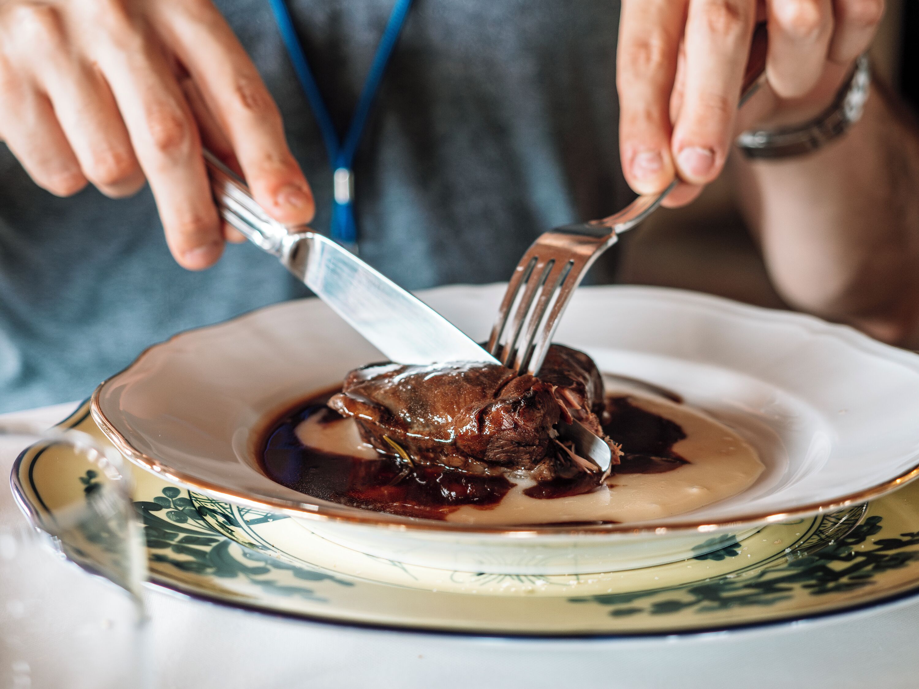 Une personne qui découpe un morceau de viande sur une assiette à l’aide d’une fourchette et d’un couteau.