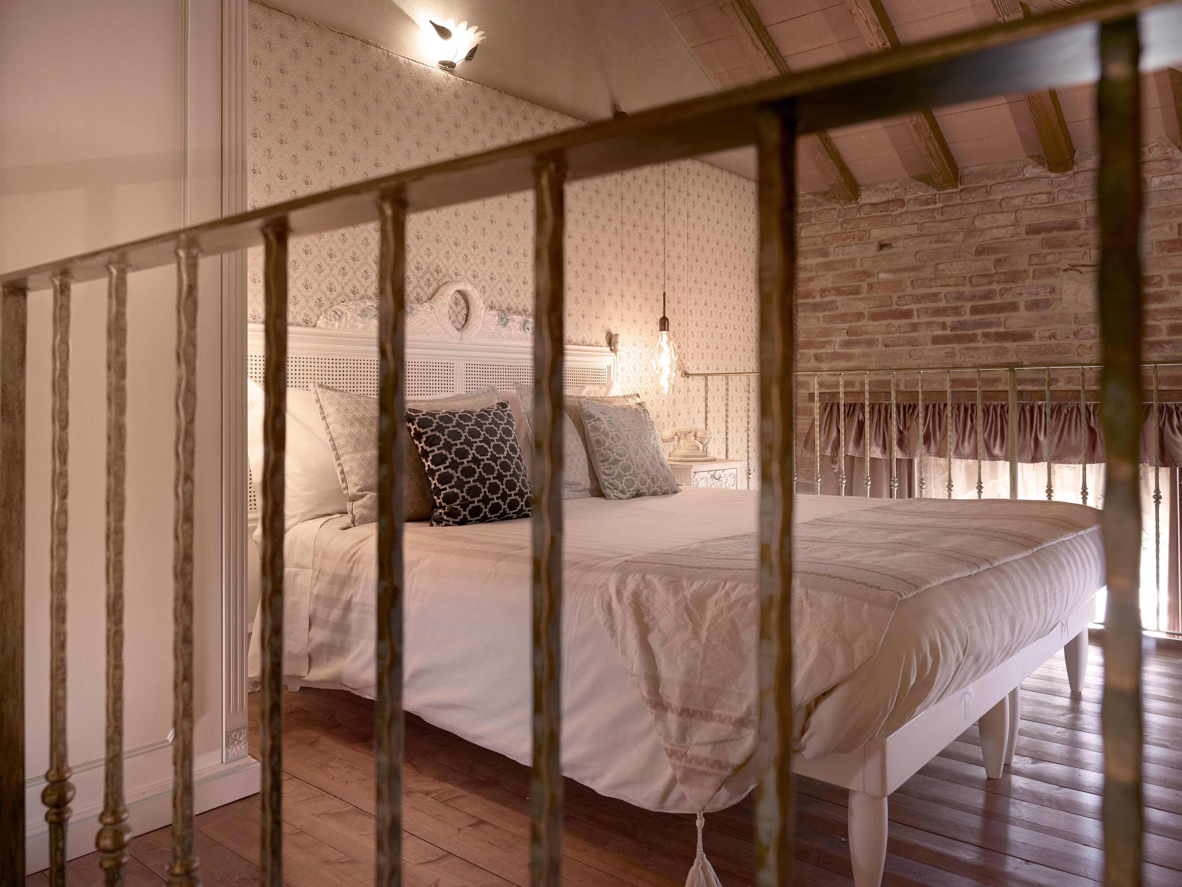 A bedroom with a bed, a wooden floor, a brick wall, and a ceiling with exposed beams.