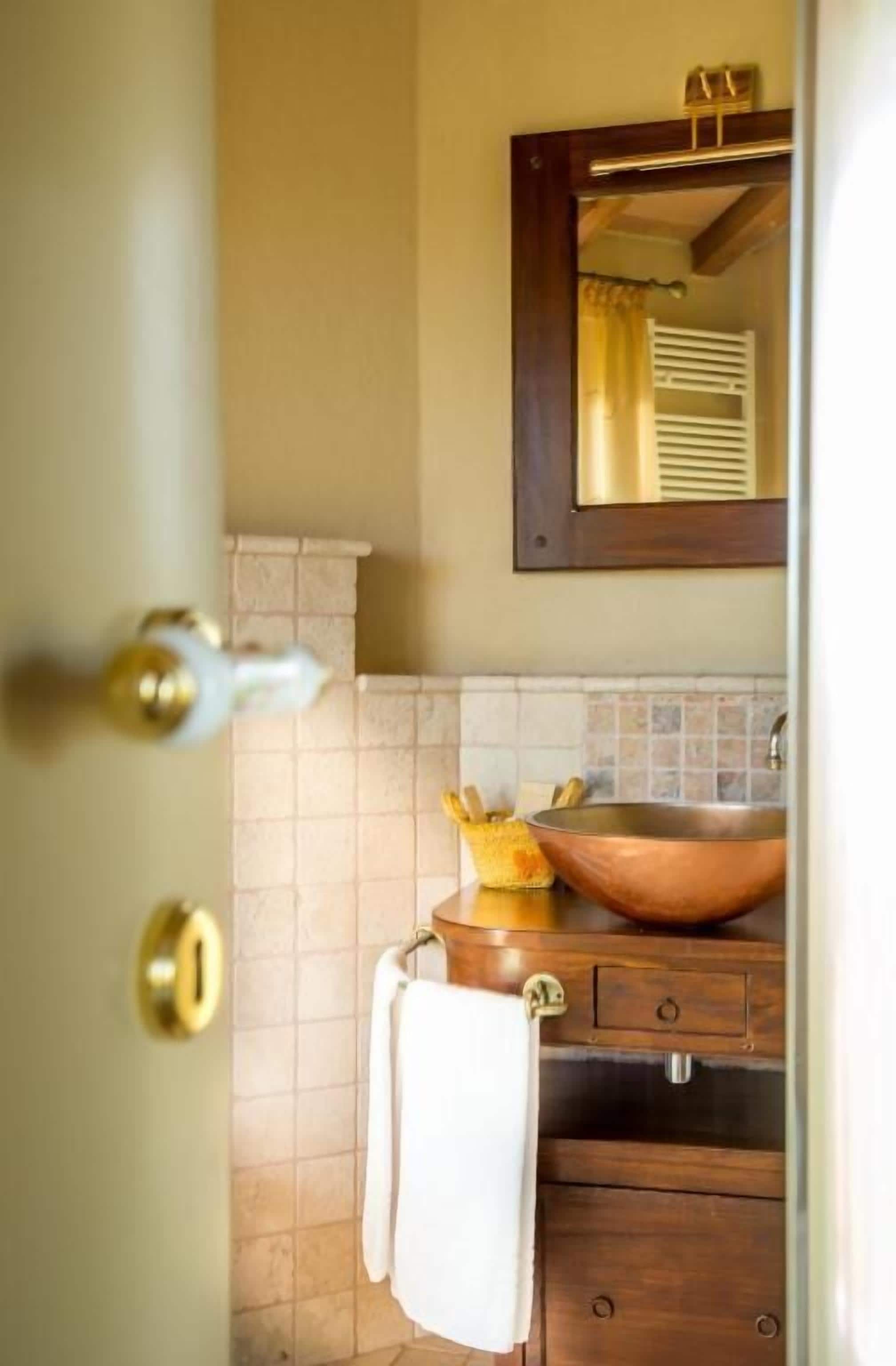 A bathroom with a wooden vanity, a copper sink, and a mirror above it.