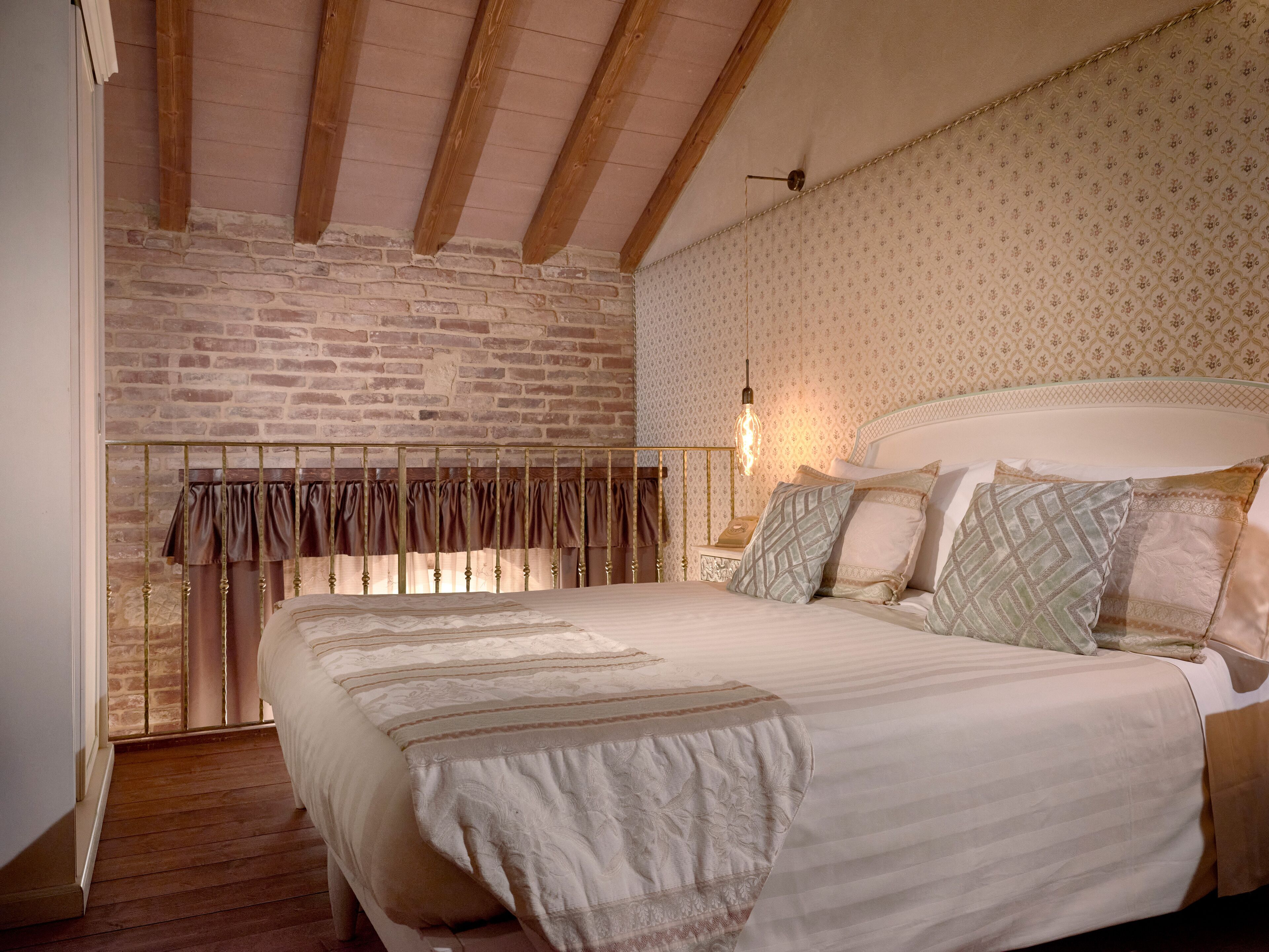Ein Schlafzimmer mit Backsteinwand, Holzboden und strukturierter Tapete, ausgestattet mit einem Bett und vielen Kissen.