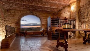 A wine cellar with a large arched window, wooden benches, and a wine rack filled with bottles. - Tenuta Montemagno (Montemagno)