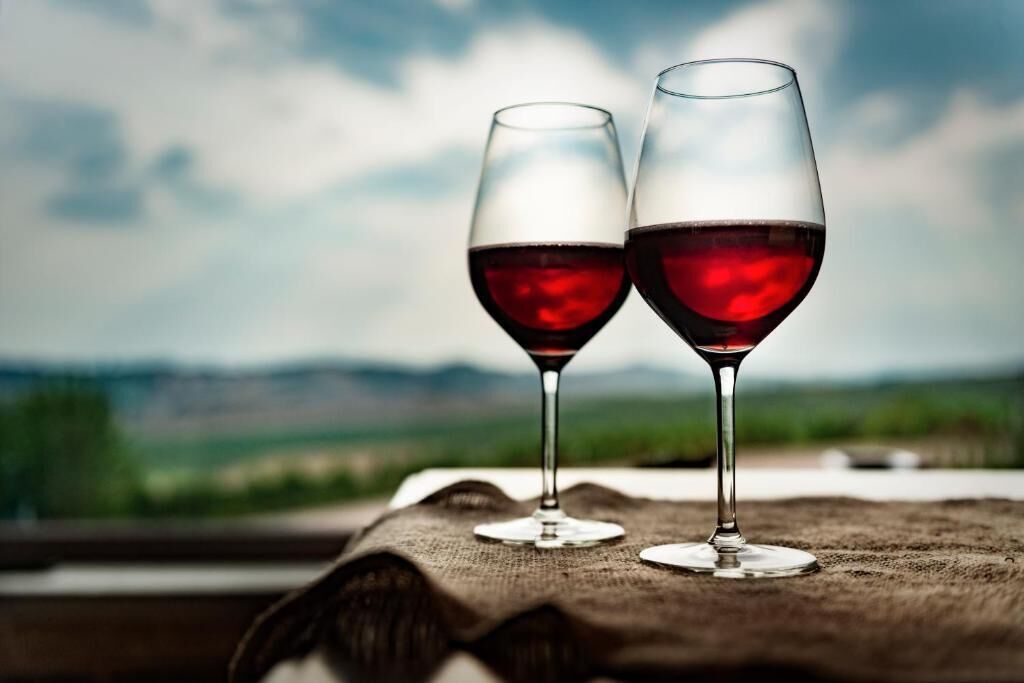 Two wine glasses on a table with a view of a landscape.