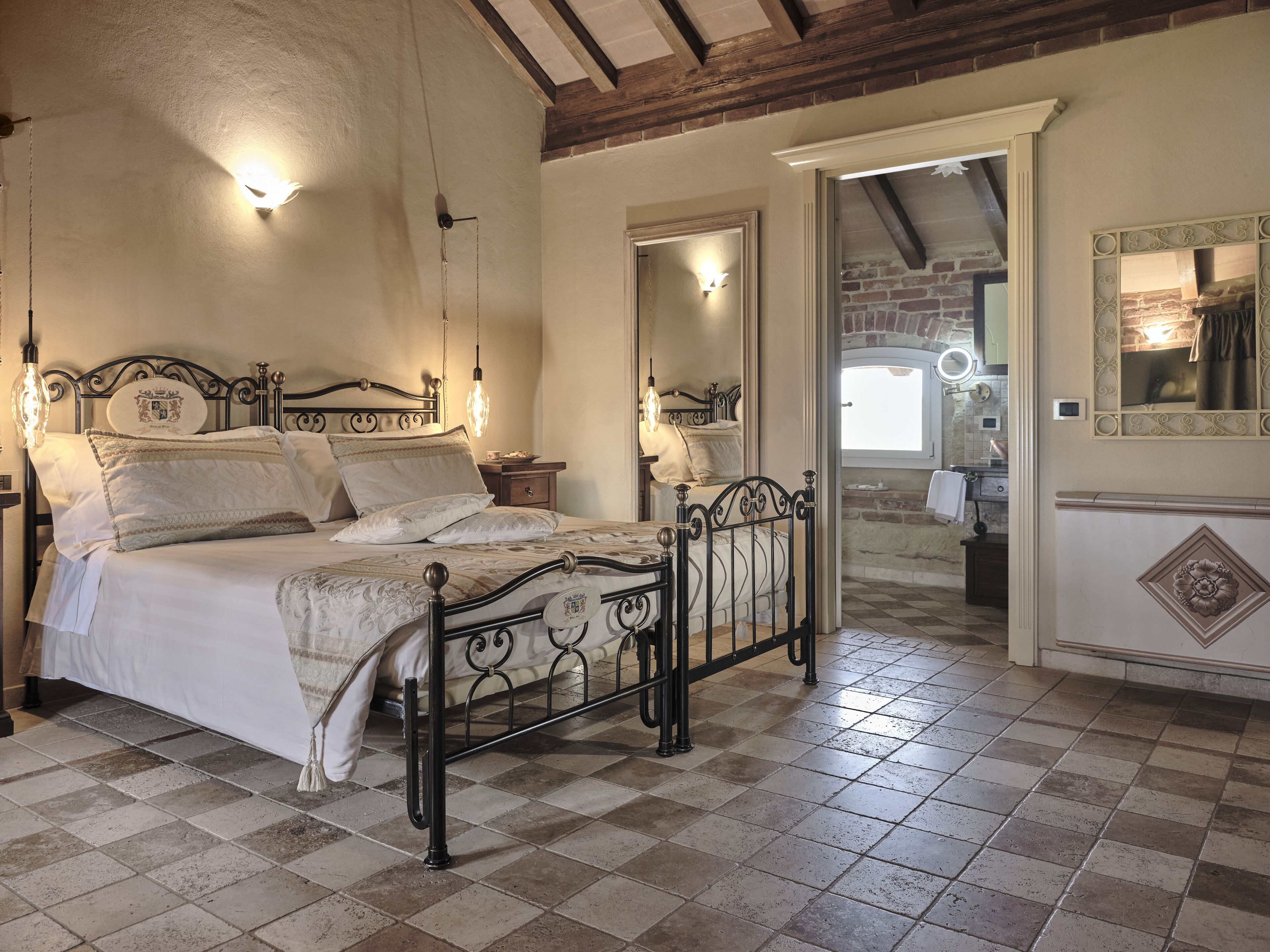 A bedroom with a four-poster bed, a nightstand, a mirror, and a view of a kitchen.