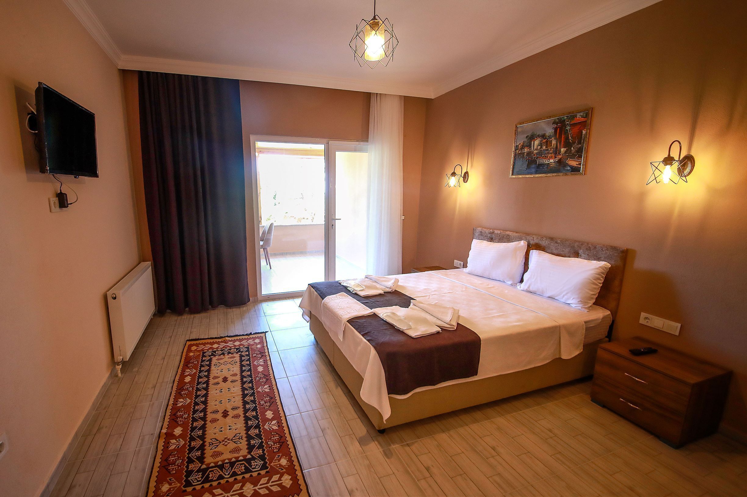 A hotel room with a large bed, a bedside table, a nightstand, a TV mounted on the wall, and a painting on the wall.