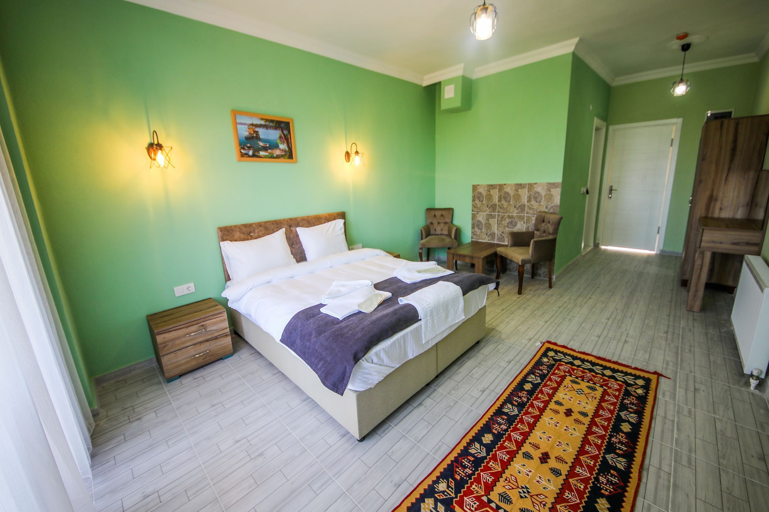 A bedroom with a bed, bedside tables, a chair, a small table, and a door.