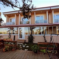 Edificio de dos pisos con un balcón en el nivel superior, una terraza de madera con plantas en macetas y una silla colgante.