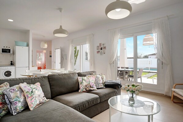 A modern living room with a grey sofa, a glass coffee table, and a view of the outdoors.
