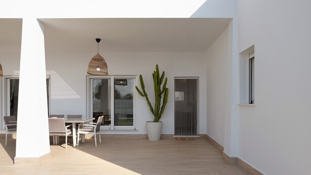 Eine moderne Terrasse mit Esstisch und Stühlen, einer großen Topf-Kaktus und einer Schiebeglastür.
