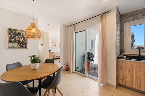Une cuisine moderne avec un coin repas, une porte-fenêtre coulissante donnant sur un balcon et une vue sur l’extérieur.