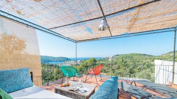 A balcony with a bed, two chairs, a table with a magazine, and a hanging light fixture. - House with Pool and Sea Views - Casa Can Divertit (Can Budella)