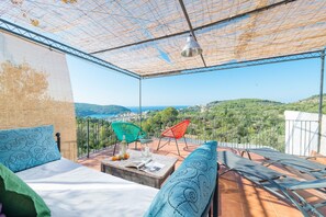 A balcony with a bed, two chairs, a table with a magazine, and a hanging light fixture.
