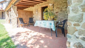 A stone building with a covered patio, outdoor seating, and a table with a tablecloth.