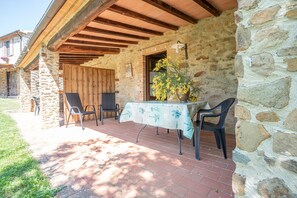 A stone building with a covered patio, outdoor seating, and a table with a tablecloth.