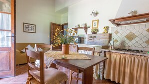 A dining area with a wooden table, chairs, a potted plant, and a kitchen area with a stove and tiled backsplash.