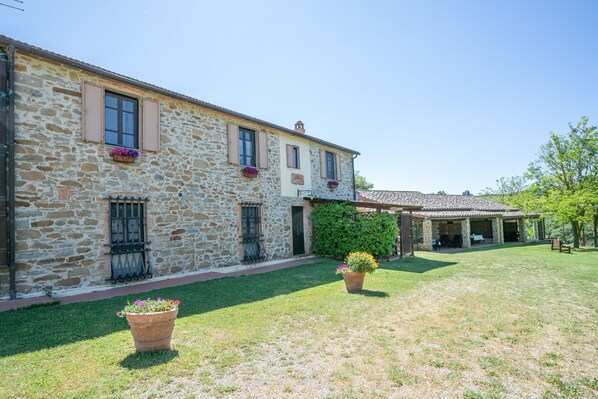 A stone building with a covered patio, a grassy lawn, and potted plants.