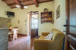 A cozy living room with a wooden ceiling, a sofa, a TV mounted on the wall, a wooden shelf with decorative items, and a stone wall.