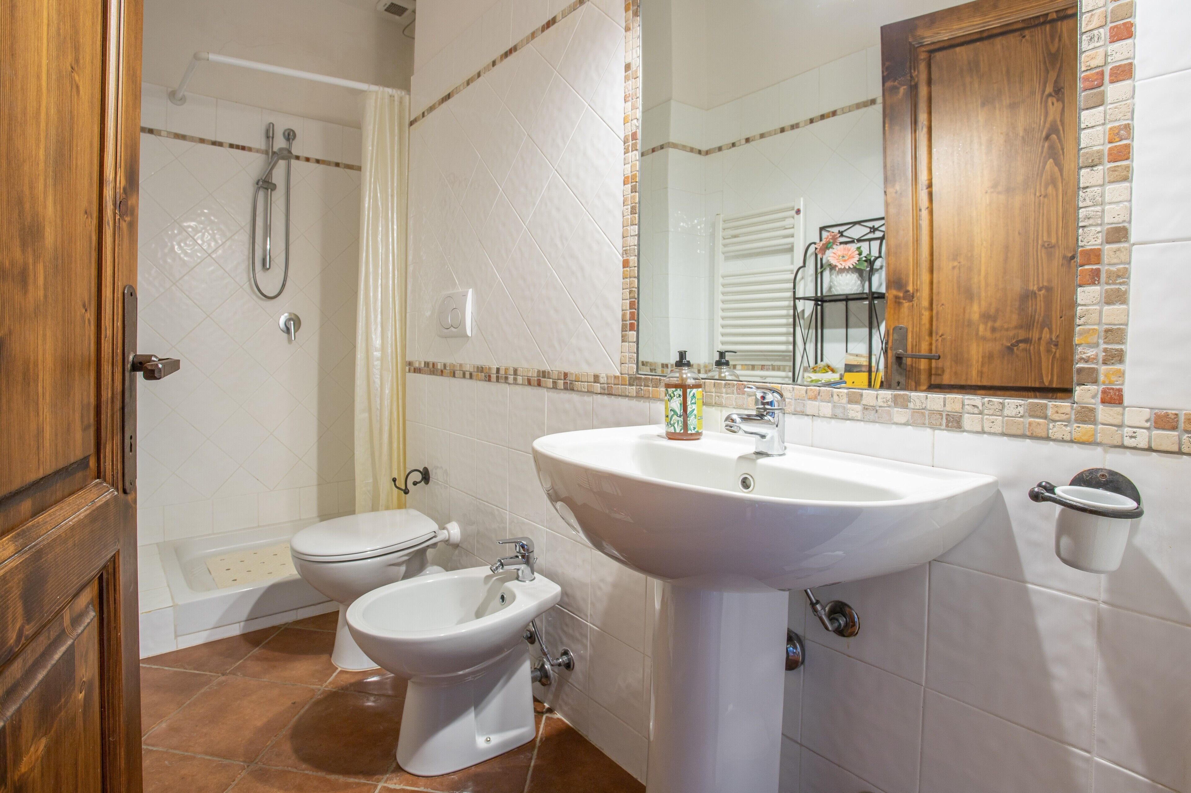 Un baño con inodoro, bidé, lavamanos, ducha y puerta de madera.