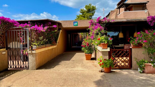 Un edificio con un letrero con el número 21, una entrada con portón y plantas en macetas con flores.