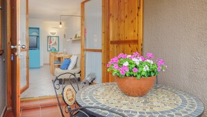 Una puerta abierta que da a un espacio de estar con una mesa con azulejos, una planta en maceta y un espejo con marco azul.