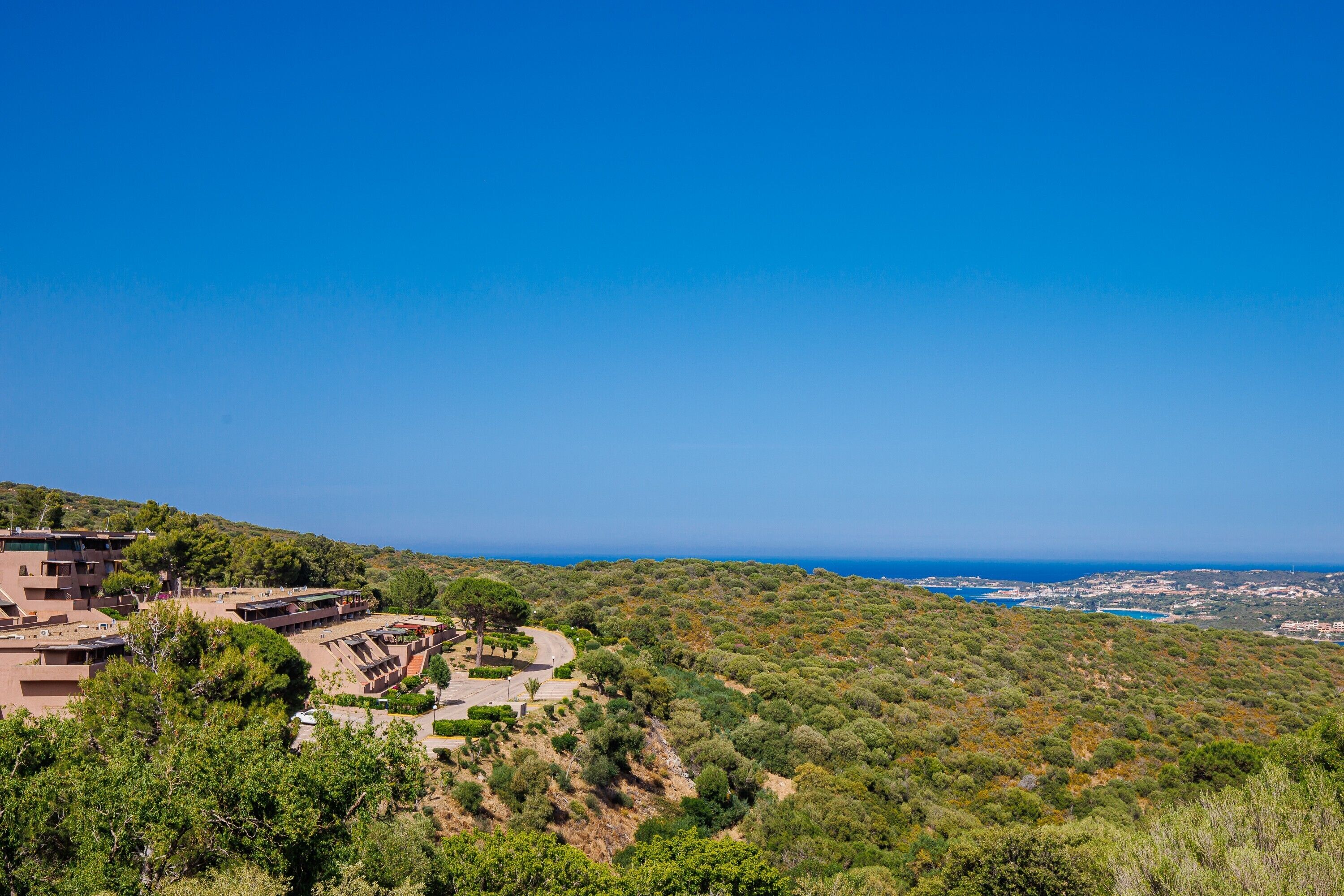 A coastal resort with a view of the sea, terraced buildings, and lush greenery.