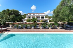 A pool with clear water, surrounded by lounge chairs and umbrellas, with a building in the background.