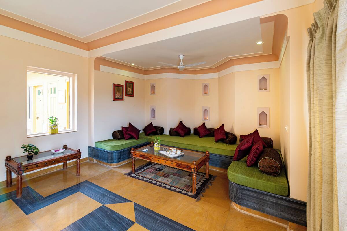 A spacious living room with a green sofa set, a wooden coffee table, and a patterned rug.