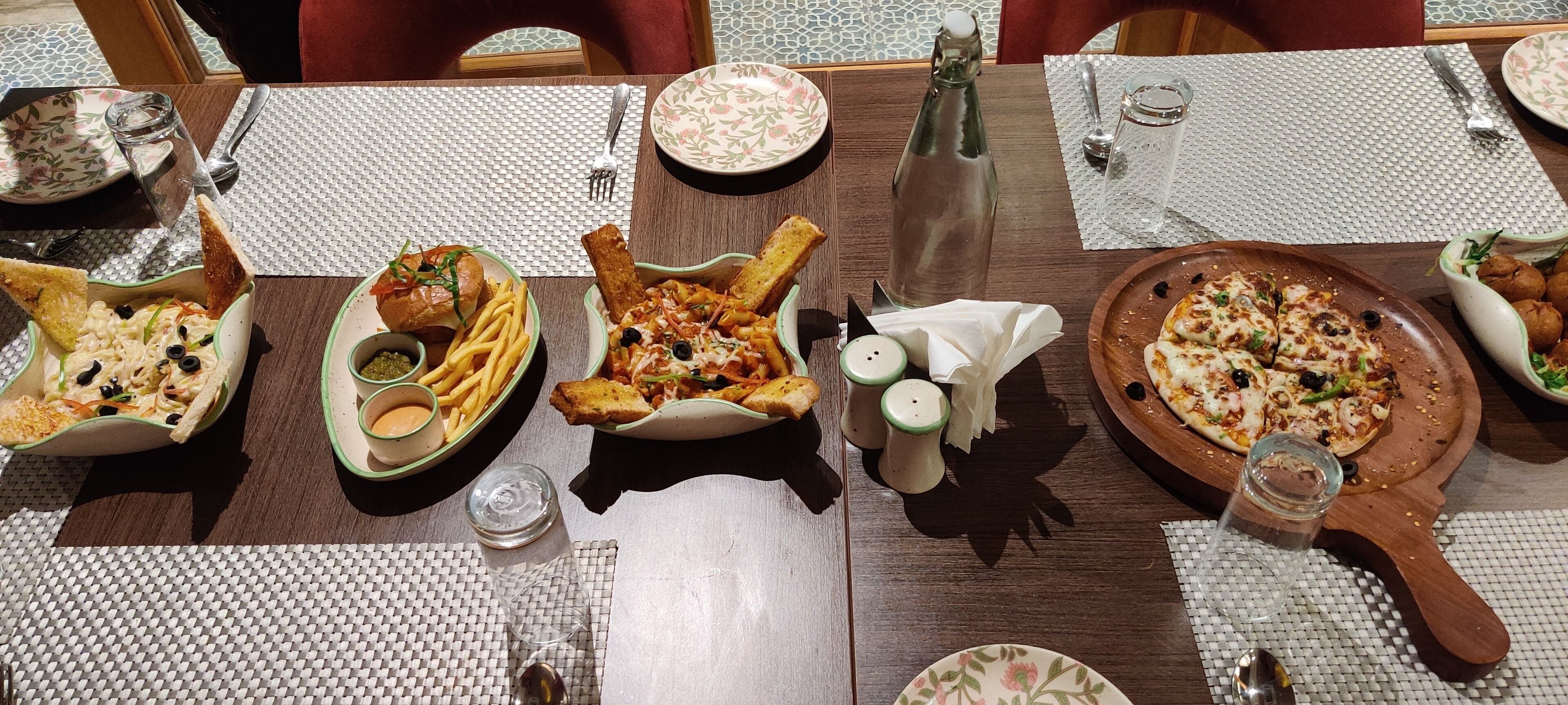 A dining table with various dishes, including pasta, fries, and pizza, along with condiments and utensils.