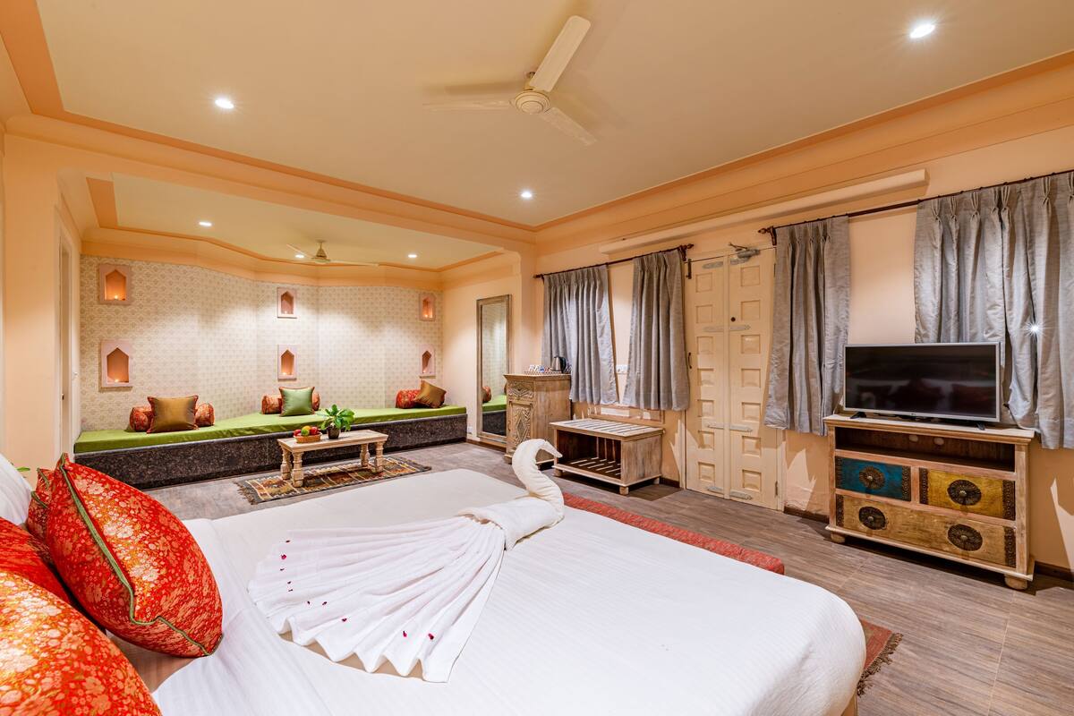 A hotel room with a bed, a television, a seating area, and a decorative swan towel on the bed.