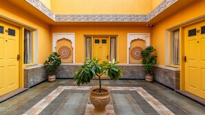 A yellow-walled corridor with ornate doors numbered 61 and 62, potted plants, and patterned tiles.