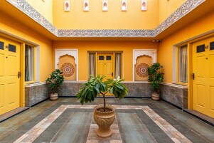 A yellow-walled corridor with ornate doors numbered 61 and 62, potted plants, and patterned tiles.