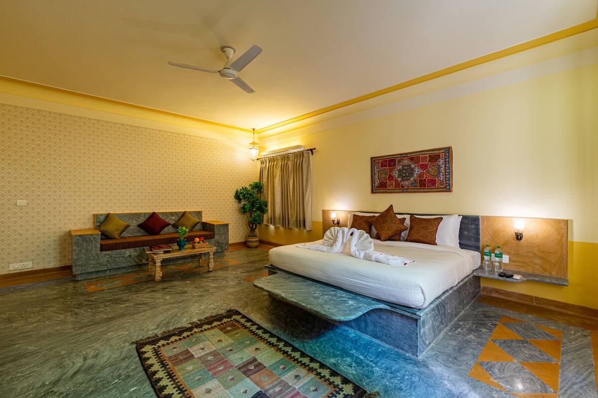 A hotel room with a bed, a sofa, a coffee table, a plant, and a patterned rug.
