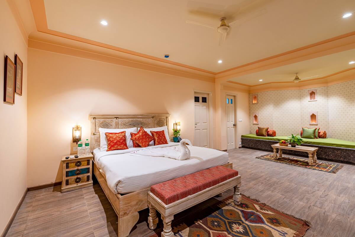 A spacious bedroom with a large bed, a bench, a nightstand, and a seating area with a green sofa and cushions.
