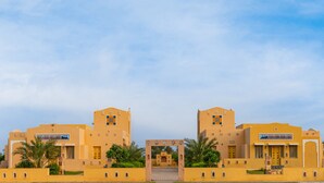 A symmetrical building with a central archway, likely a hotel entrance, surrounded by palm trees and a clear sky.