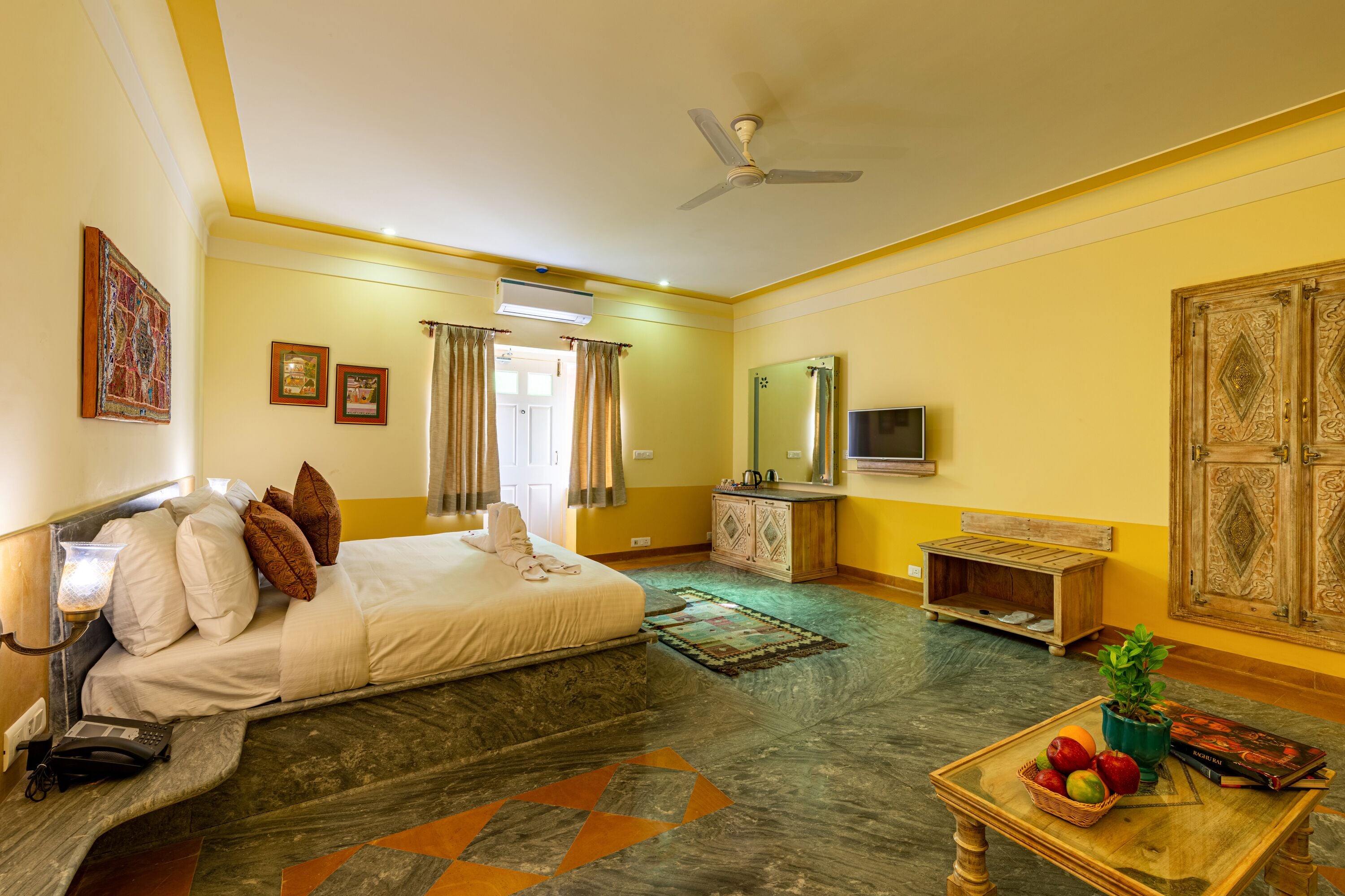 A hotel room with a bed, a desk, a television, and a small table with fruit.