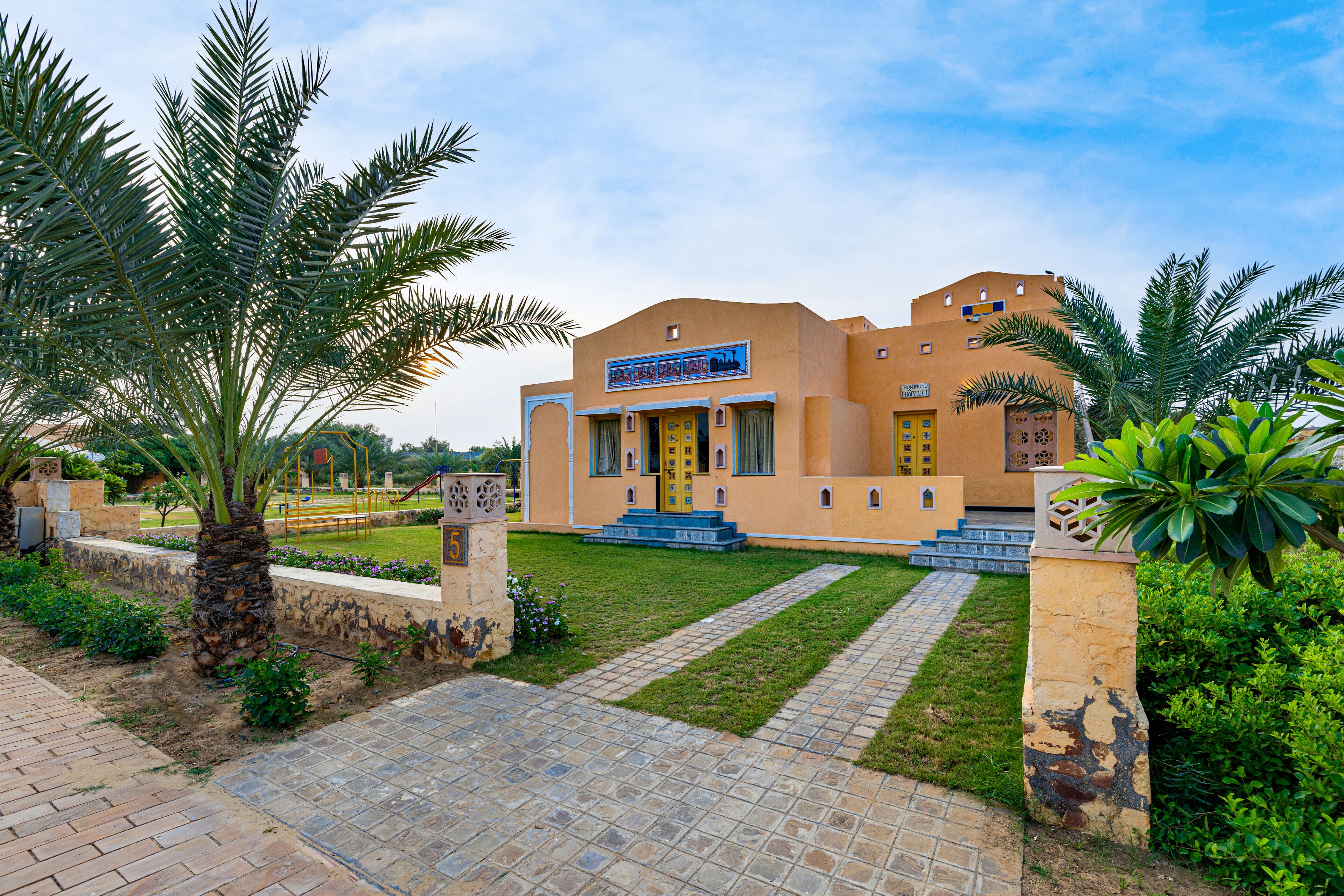 A building with a traditional architectural style, featuring a central entrance with steps, surrounded by palm trees and a well-maintained lawn.