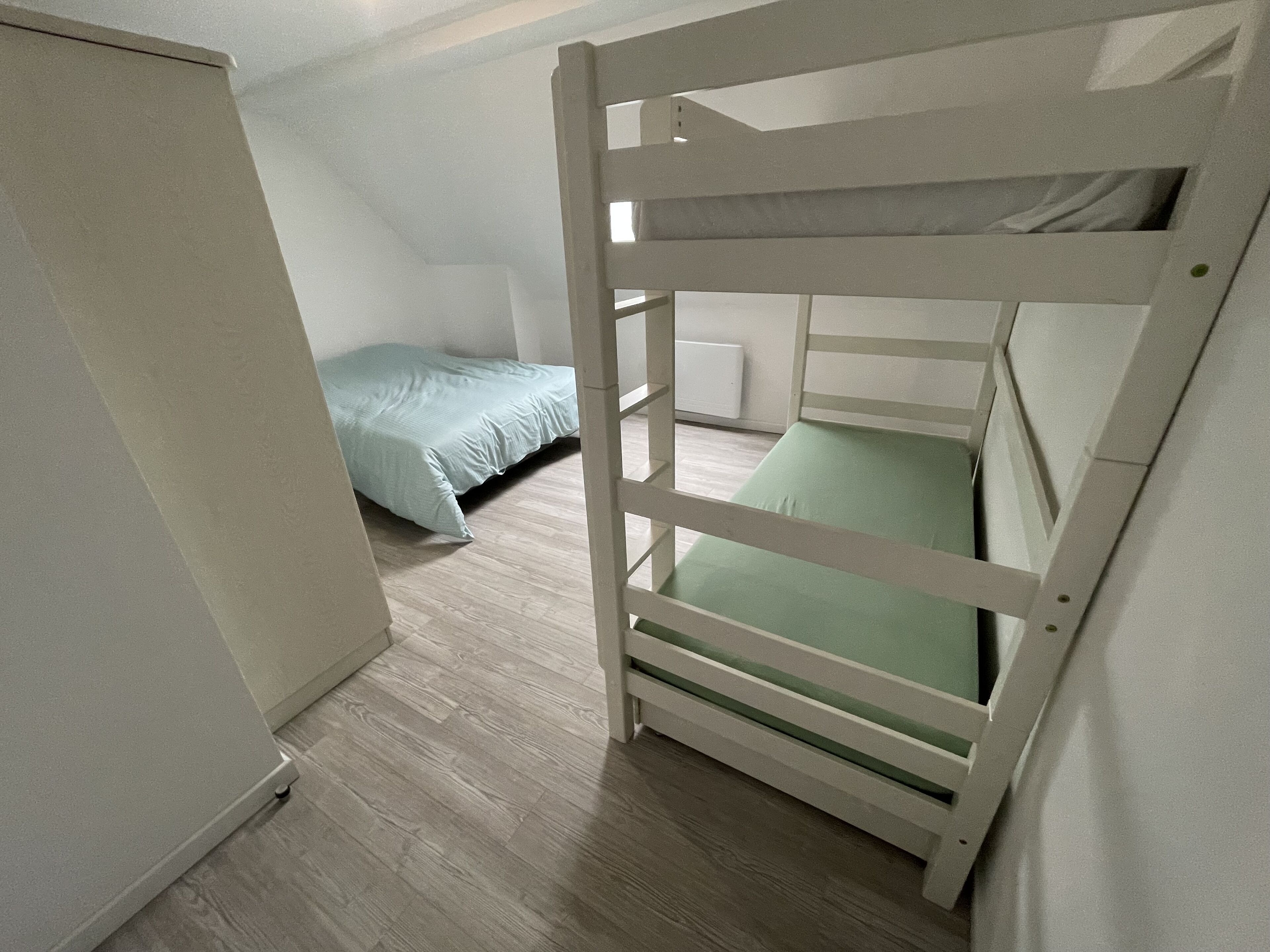 A bunk bed with a green mattress and a single bed with a light blue mattress in a room with wooden flooring and white walls.