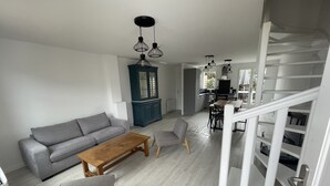 Una sala de estar moderna con un sofá gris, una mesa de centro de madera y un sillón gris. Se ve una escalera con baranda blanca que sube a un segundo piso.