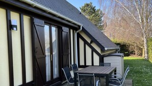 A covered patio with a table and chairs, a garage, and a grassy area with trees.