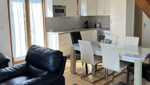 A modern kitchen with white cabinets, a dining table with chairs, and a black leather sofa.