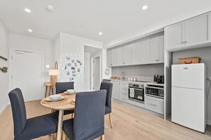 A modern kitchen with white cabinets, a dining area with a table and chairs, and a refrigerator.