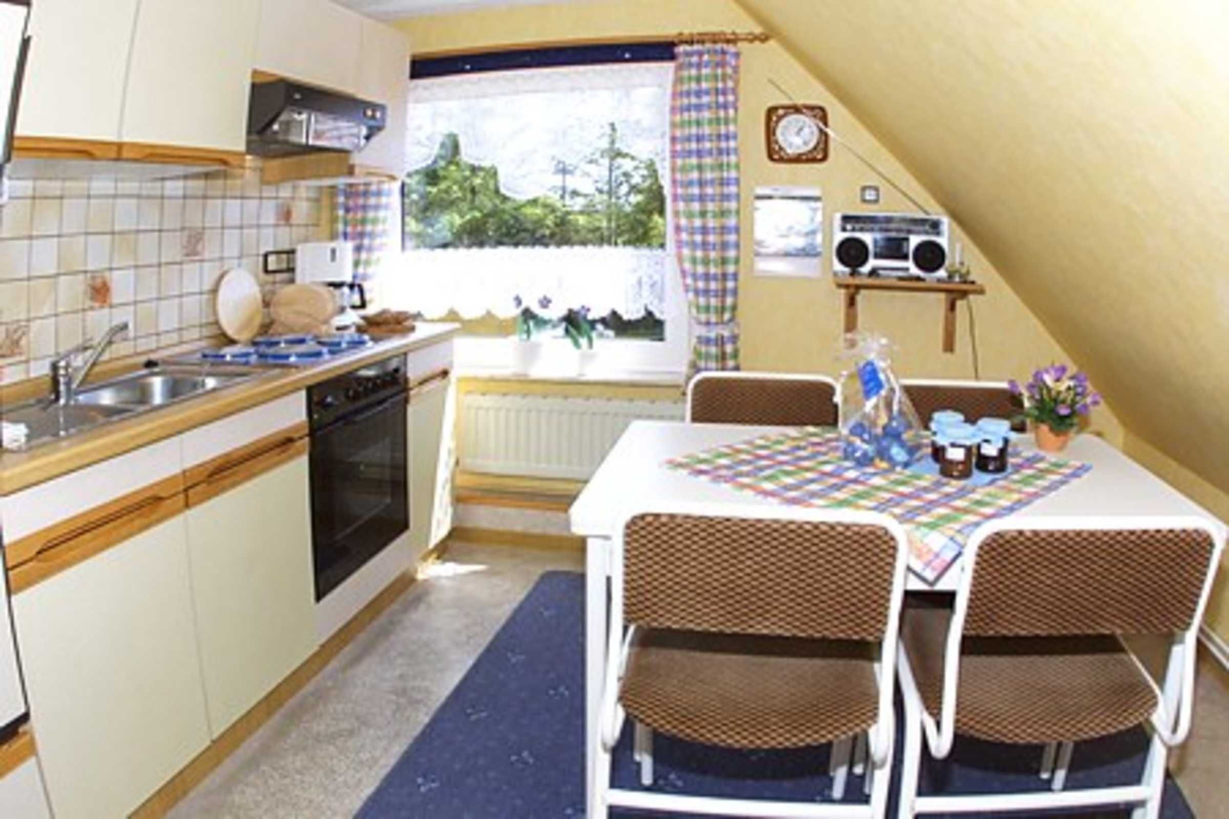 Una cocina con ventana, una mesa con sillas, un radio y un reloj en la pared.