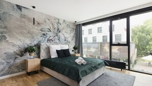 Un dormitorio moderno con una cama grande, vistas a la ciudad a través de un ventanal amplio y un mural con textura en la pared.