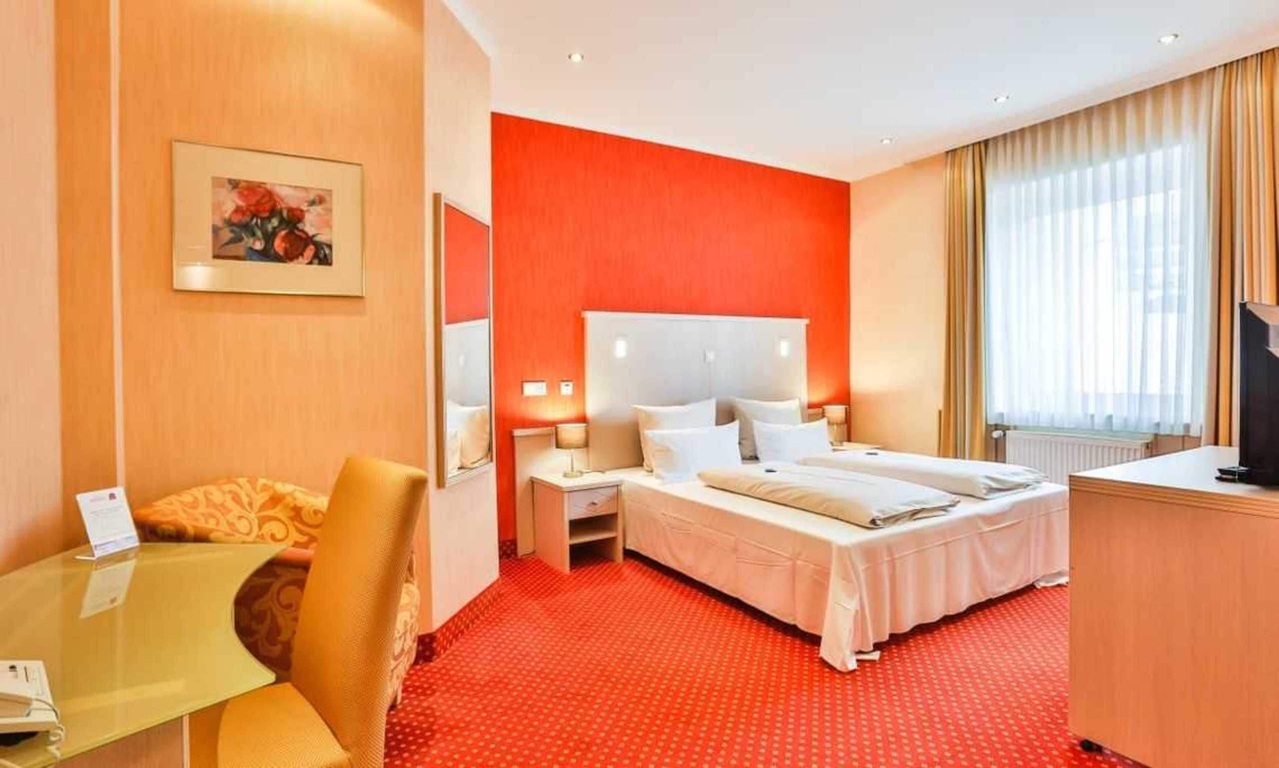 Een hotelkamer met een rood tapijt, twee bedden, een bureau en een televisie.