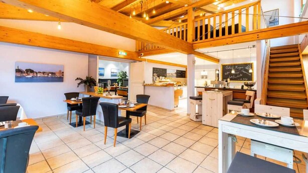 A spacious dining area with a high ceiling and wooden beams, a kitchen area with a chalkboard menu, and a staircase leading to an upper level.