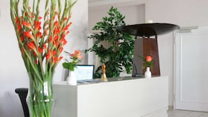 A reception desk with a computer, a vase with flowers, and a potted plant.