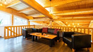 A cozy loft-style room with a wooden ceiling, a black leather sofa, a wooden coffee table, and a wooden railing.