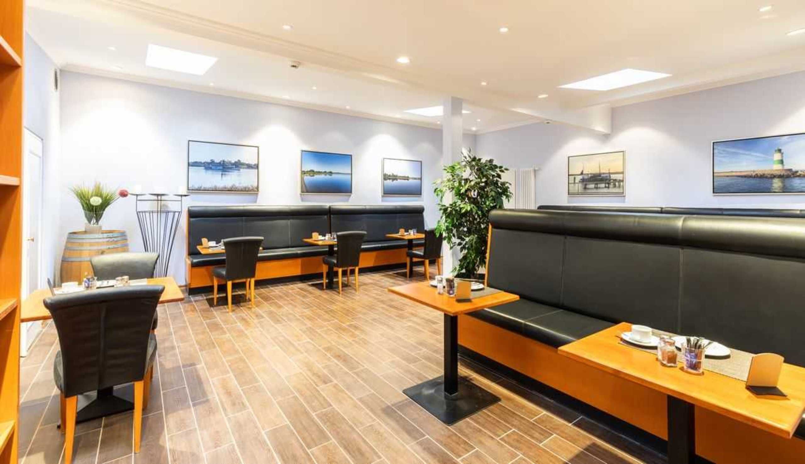 En restaurant med moderne interiør, sorte læderbænke, træborde og et fliset gulv.